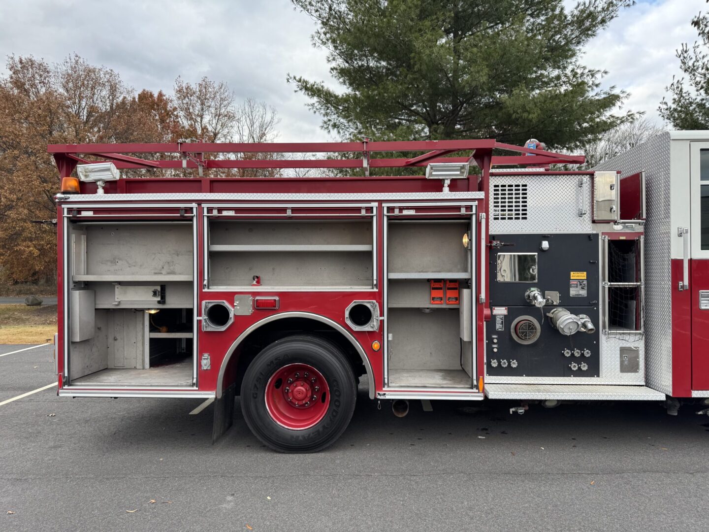 Officer’s side of a 2008 Pierce Contender pumper with its compartment doors open, showing empty shelving and the pump panel.